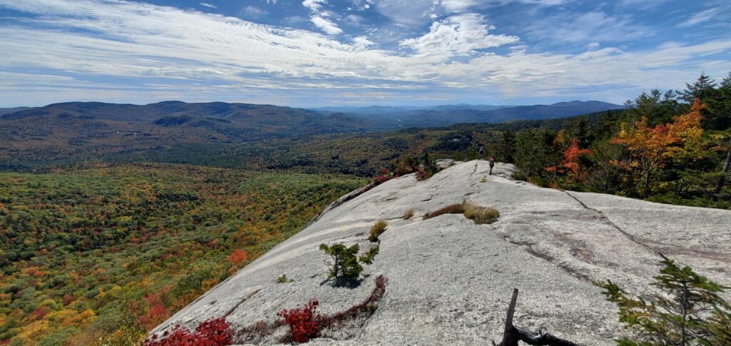 Hikers moving along granite rock face above the tree line of the Welch-Dickey loop.